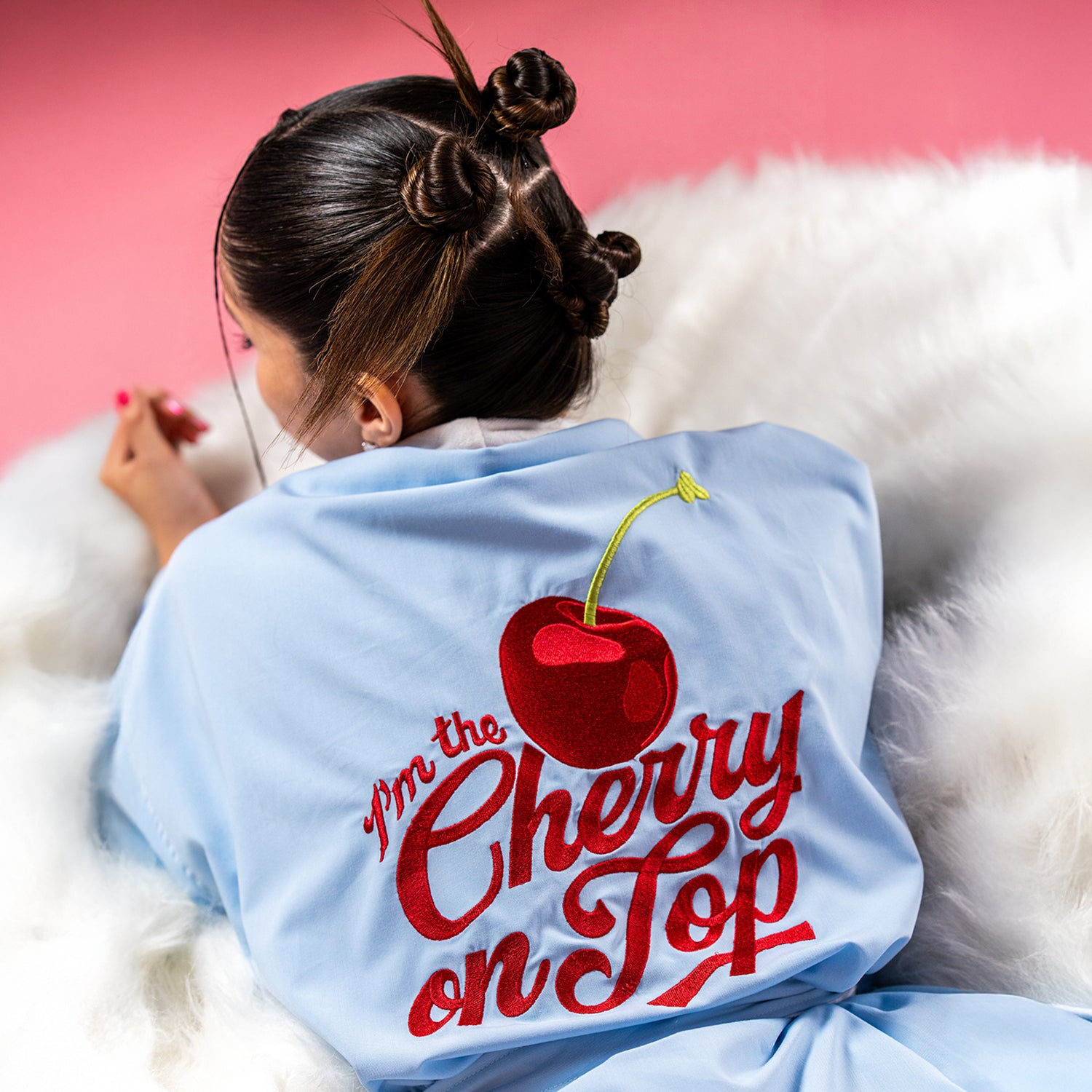 Model wearing a light blue spa robe with red cherry embroidery and “I’m the Cherry on Top” text, photographed against a pink background
